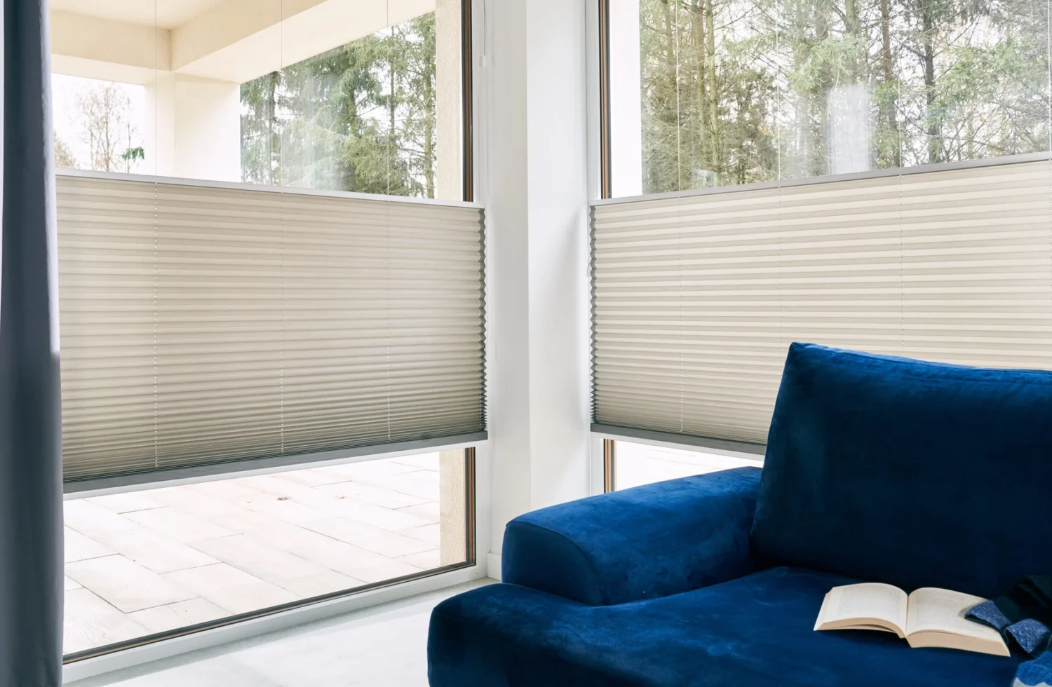 Moderner Wohnbereich mit blauen Sofa und halb geschlossenen Plissees an großen Fenstern